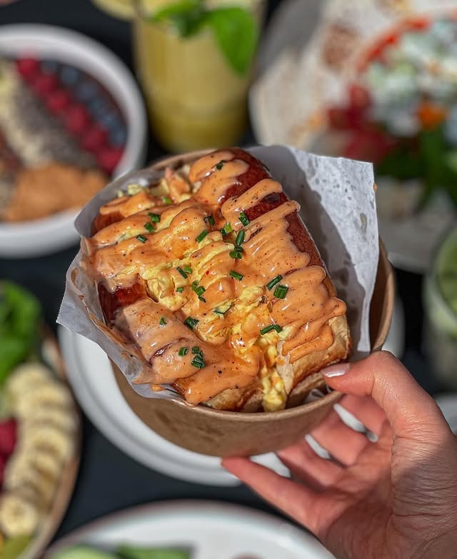 Hand hält ein saftiges Eggdrop Sandwich mit cremiger Soße und Schnittlauch beim Brunch im 9 TO 5 Berlin