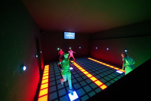 Gruppe Kinder spielt in einem abgedunkelten Raum auf beleuchtetem Boden bei den Pixel Games von Rage Axe Weiterstadt