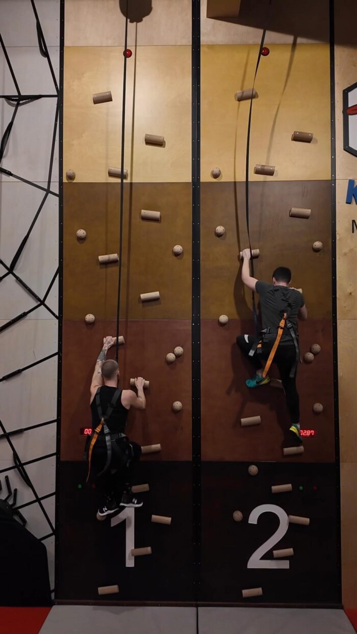 Zwei Personen beim Klettern an einer vertikalen Kletterwand mit Sicherungsgurten, Fokus auf Schnelligkeit