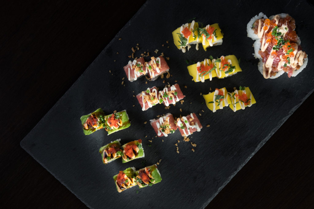 Bunte Sushi-Variation auf schwarzer Schieferplatte, mit Mango, Thunfisch, Avocado und verschiedenen Toppings wie Mayonnaise, Kaviar und Kräutern