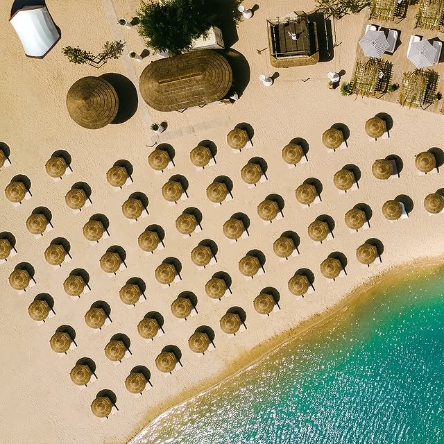 Strandbereich des Chamäleon am See in Raunheim aus der Vogelperspektive mit dutzenden Sonnenschirmen auf hellem Sand direkt am türkisblauen Wasser