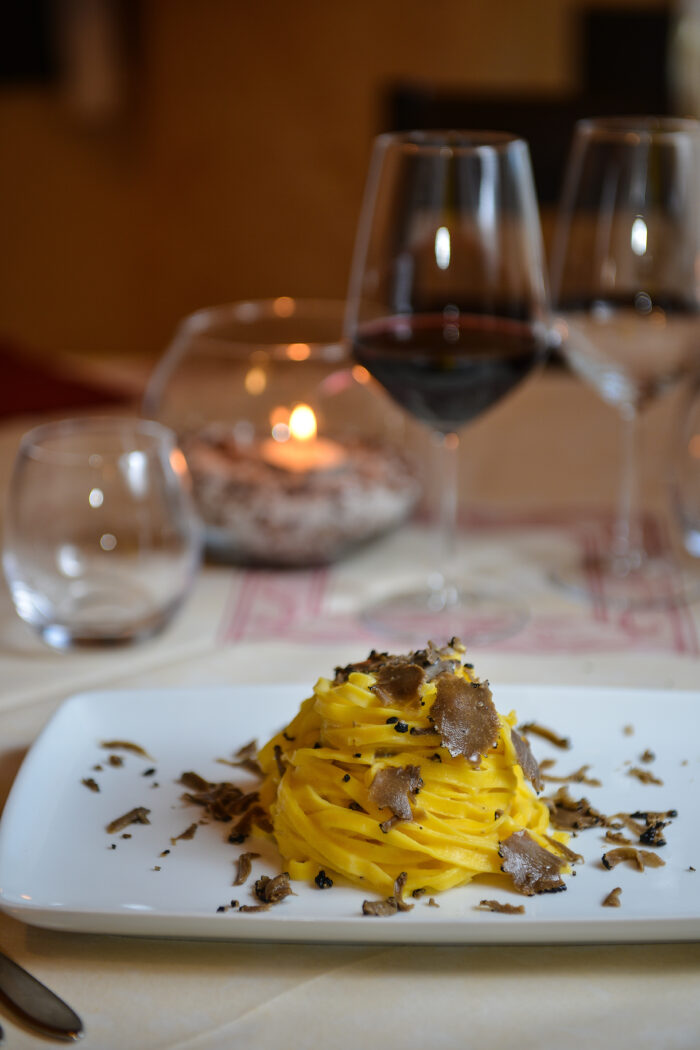 Tagliolini mit frischem Trüffel auf weißem Teller, serviert mit Rotwein im edlen Ambiente