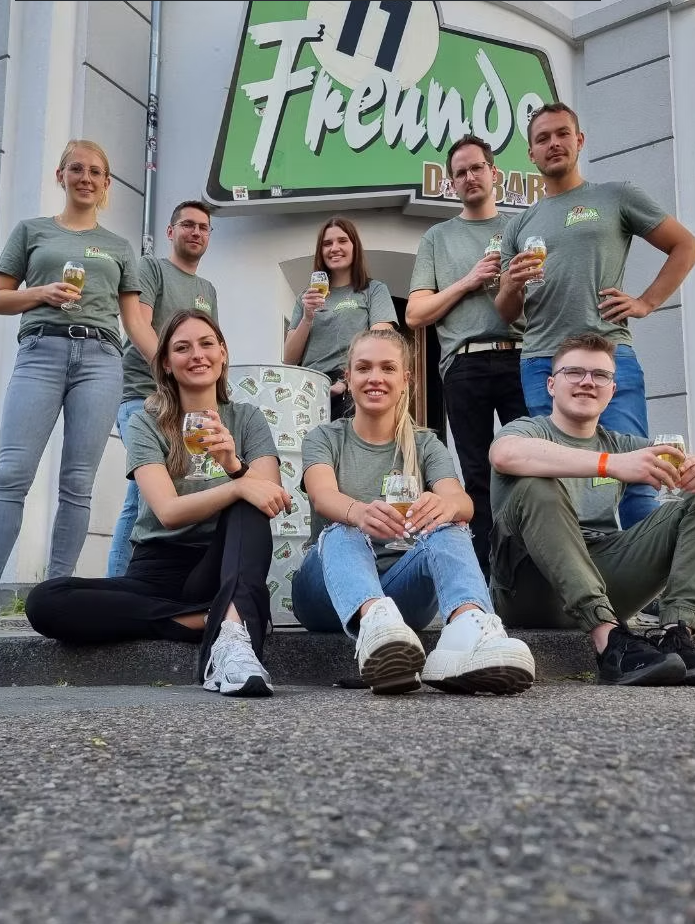 Team der 11 Freunde Bar Essen vor dem Eingang mit Bier in der Hand
