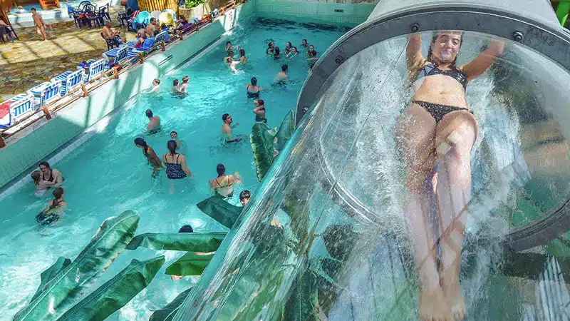 Besucherin rutscht durch transparente Glasröhre über dem Wasserbecken im Aquamagis Plettenberg