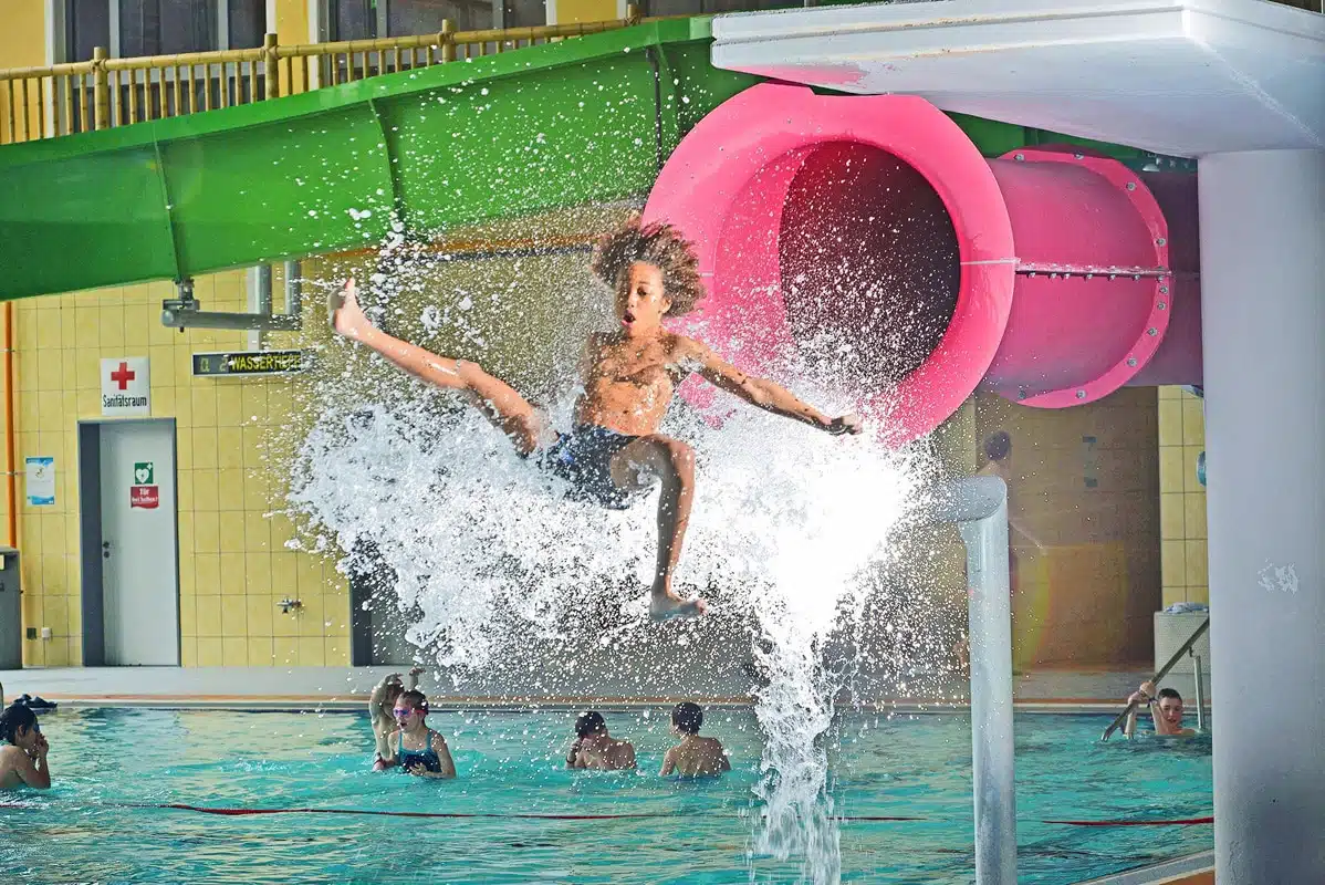 Kind springt ins Wasser vor bunter Rutsche im Aquamagis Plettenberg
