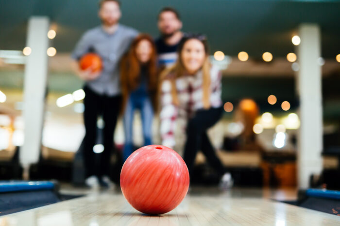 Gruppe von vier Personen beim Bowling, Fokus auf rote Bowlingkugel auf der Bahn