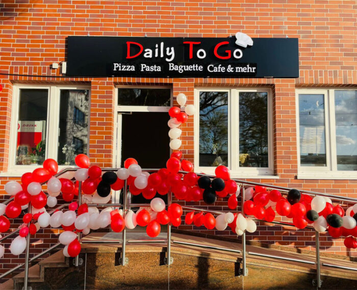 Feierlich geschmückter Eingang der Pizzaria Daily To Go in Düsseldorf mit roten und weißen Ballons