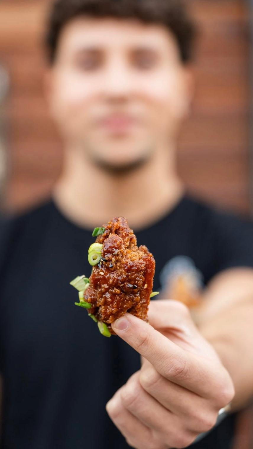 Person hält ein Stück Korean Fried Chicken in der Hand und präsentiert das knusprig glasierte Gericht bei Der Holländer in Düsseldorf.