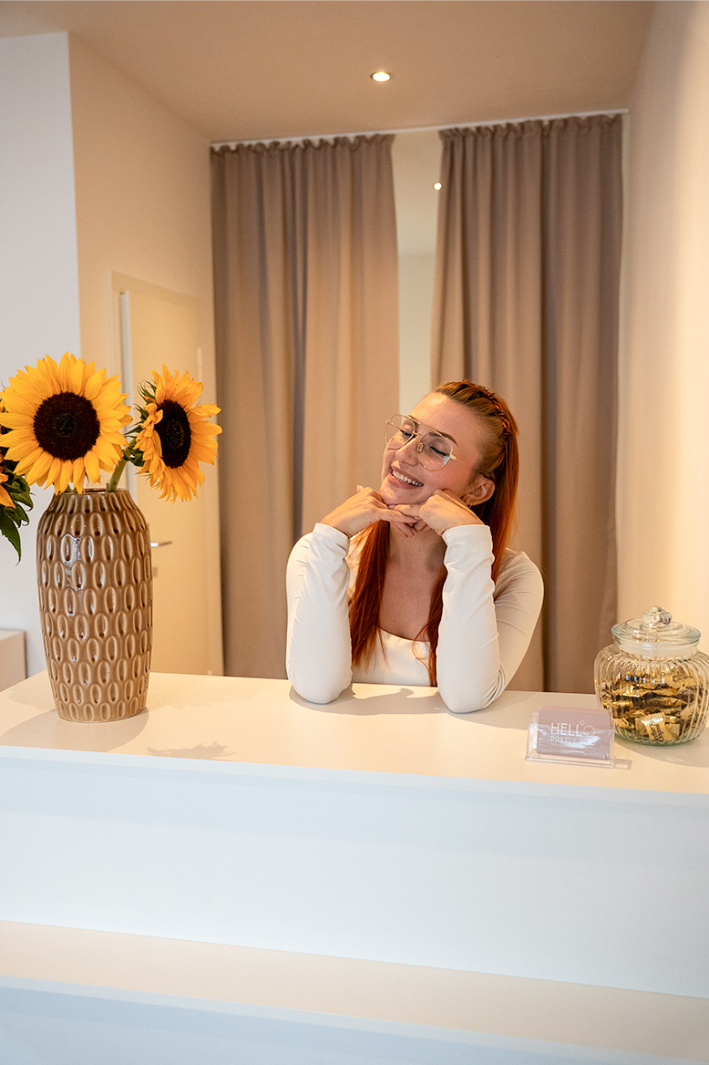 Inhaberin von Hello Pretty You in Dortmund lächelt entspannt hinter dem Tresen in einem hellen und stilvollen Studio.