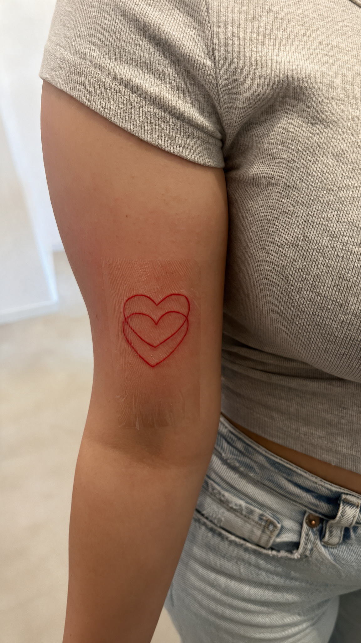 Fine Line Tattoo bei Eljo Aesthetics in Unna mit rotem Herzmotiv am Oberarm als Beispiel für ein dezentes Tattoo Motiv