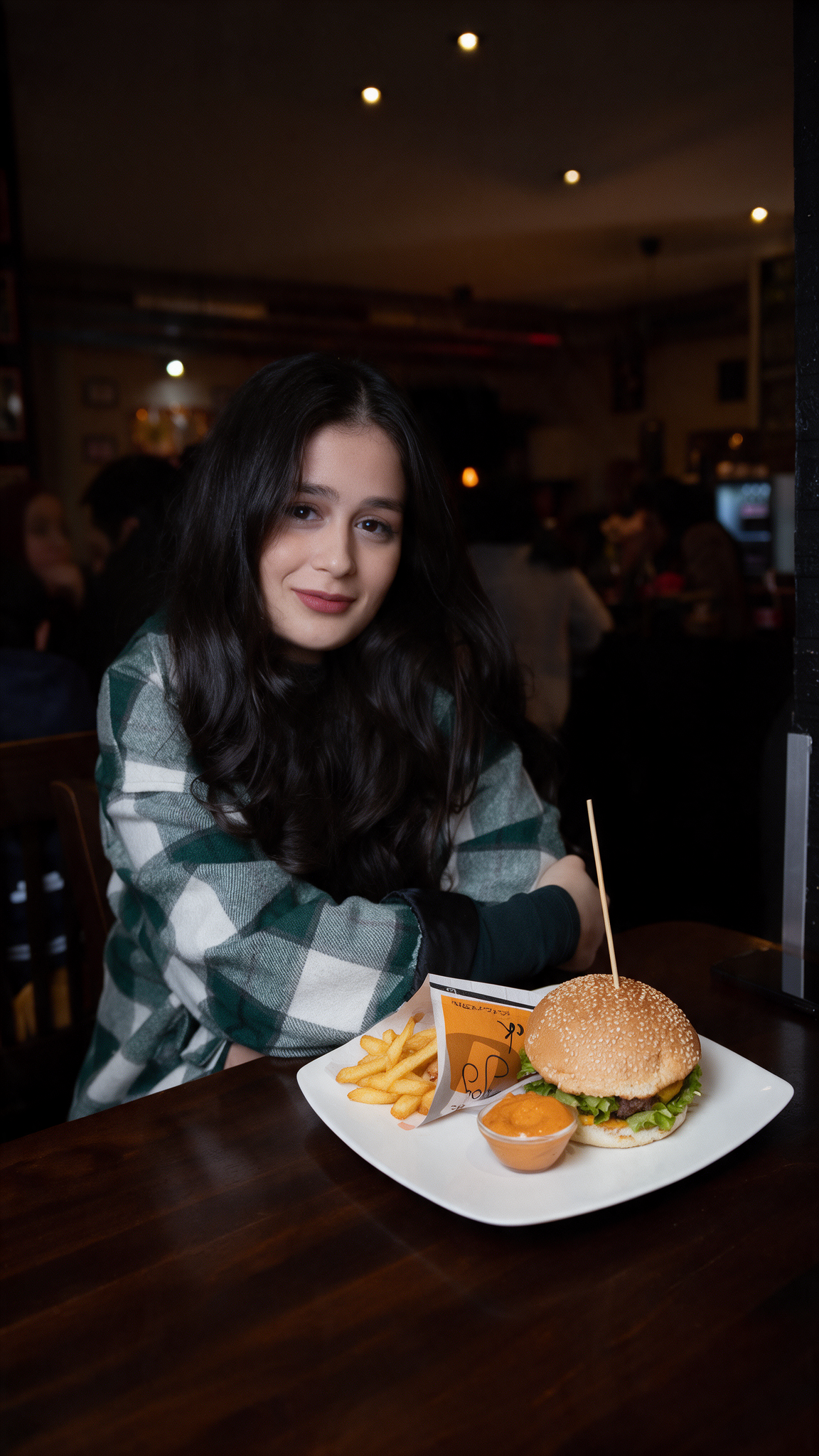 Burgermenü bei RnBeef in Düsseldorf mit einer Kundin am Tisch, frisch serviertem Burger, Pommes und Dip auf einem Teller