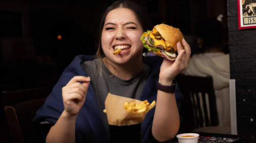 Burgermenü bei RnBeef in Essen mit Person, die einen frisch servierten Burger hält und Pommes aus einer Tüte isst